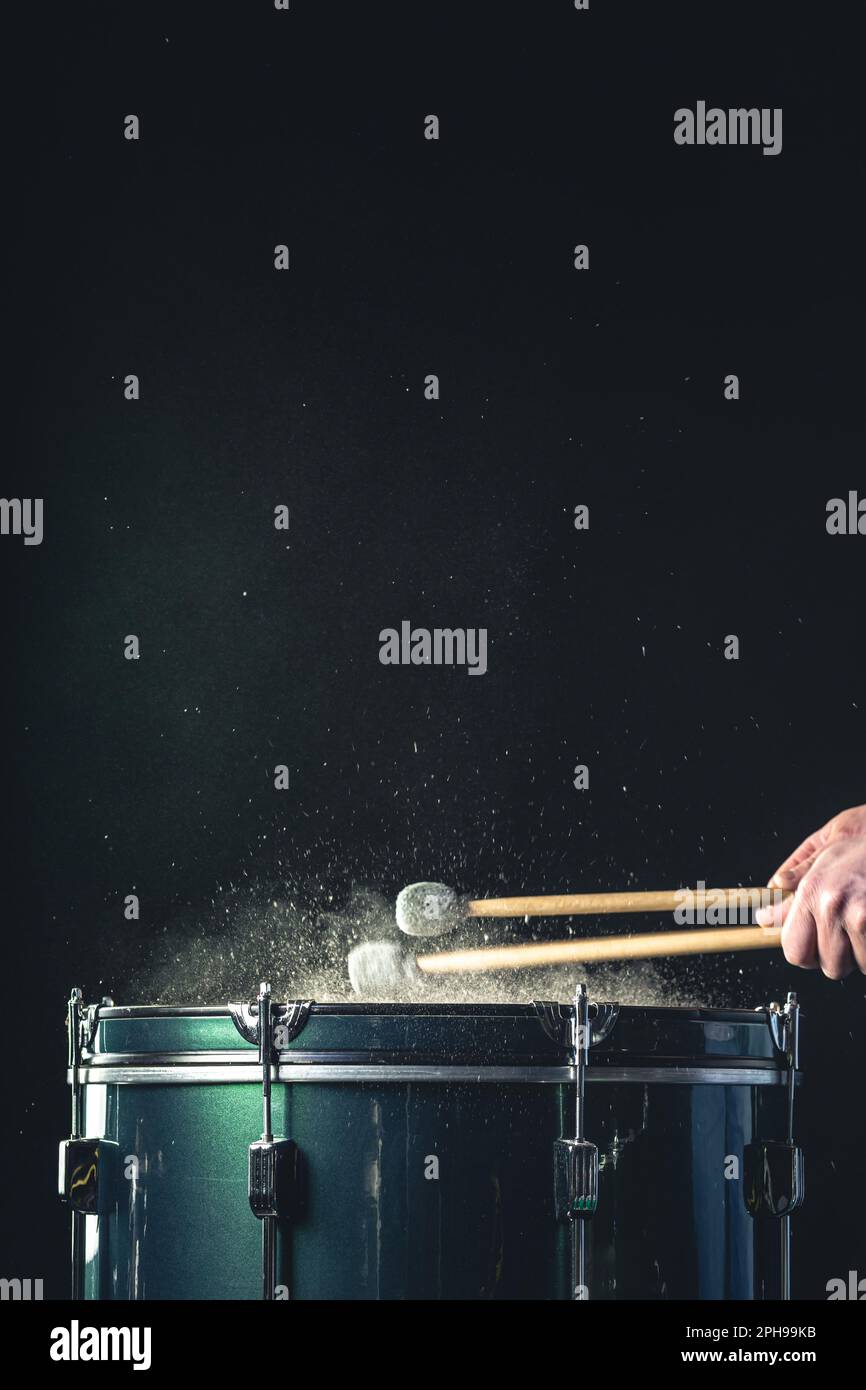 Ein Mann spielt ein musikalisches Schlaginstrument mit Stöcken auf dunklem Hintergrund. Stockfoto