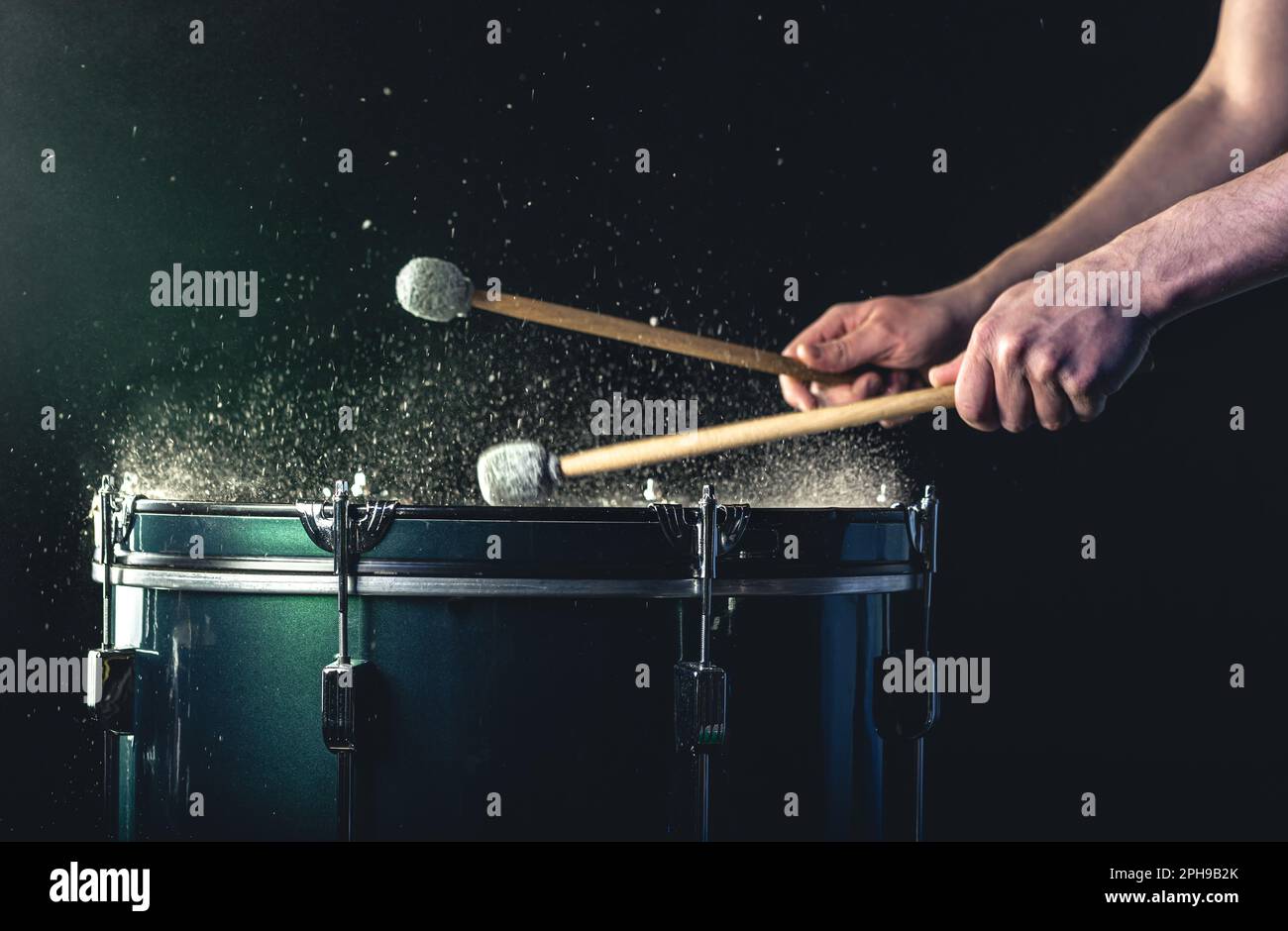 Ein Mann spielt ein musikalisches Schlaginstrument mit Stöcken auf dunklem Hintergrund. Stockfoto