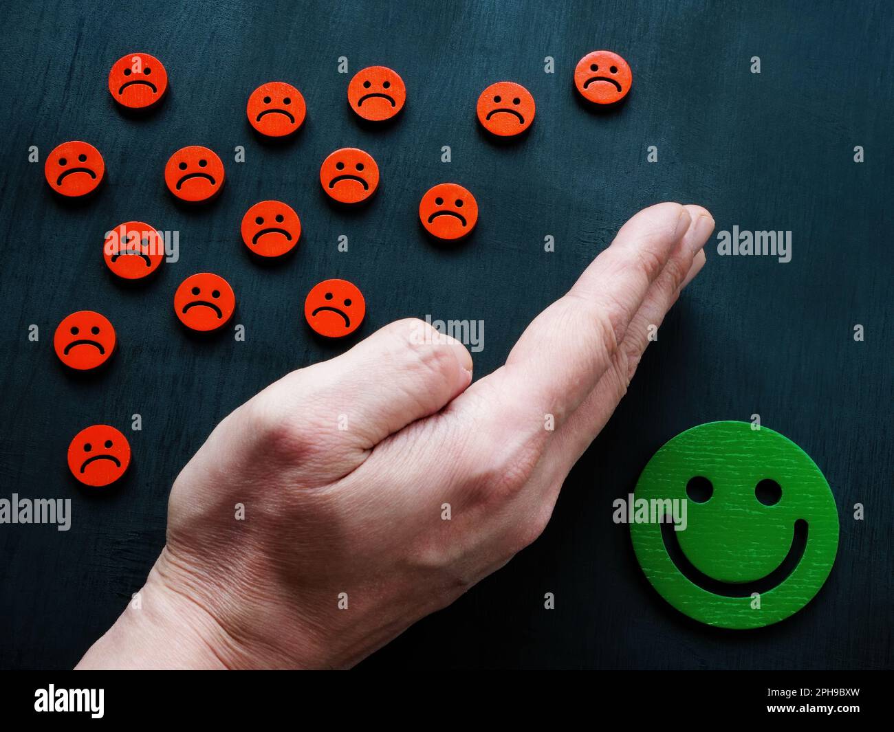 Die Hand schützt die freudigen Emotikone vor den traurigen. Emotionales Regelungskonzept. Stockfoto