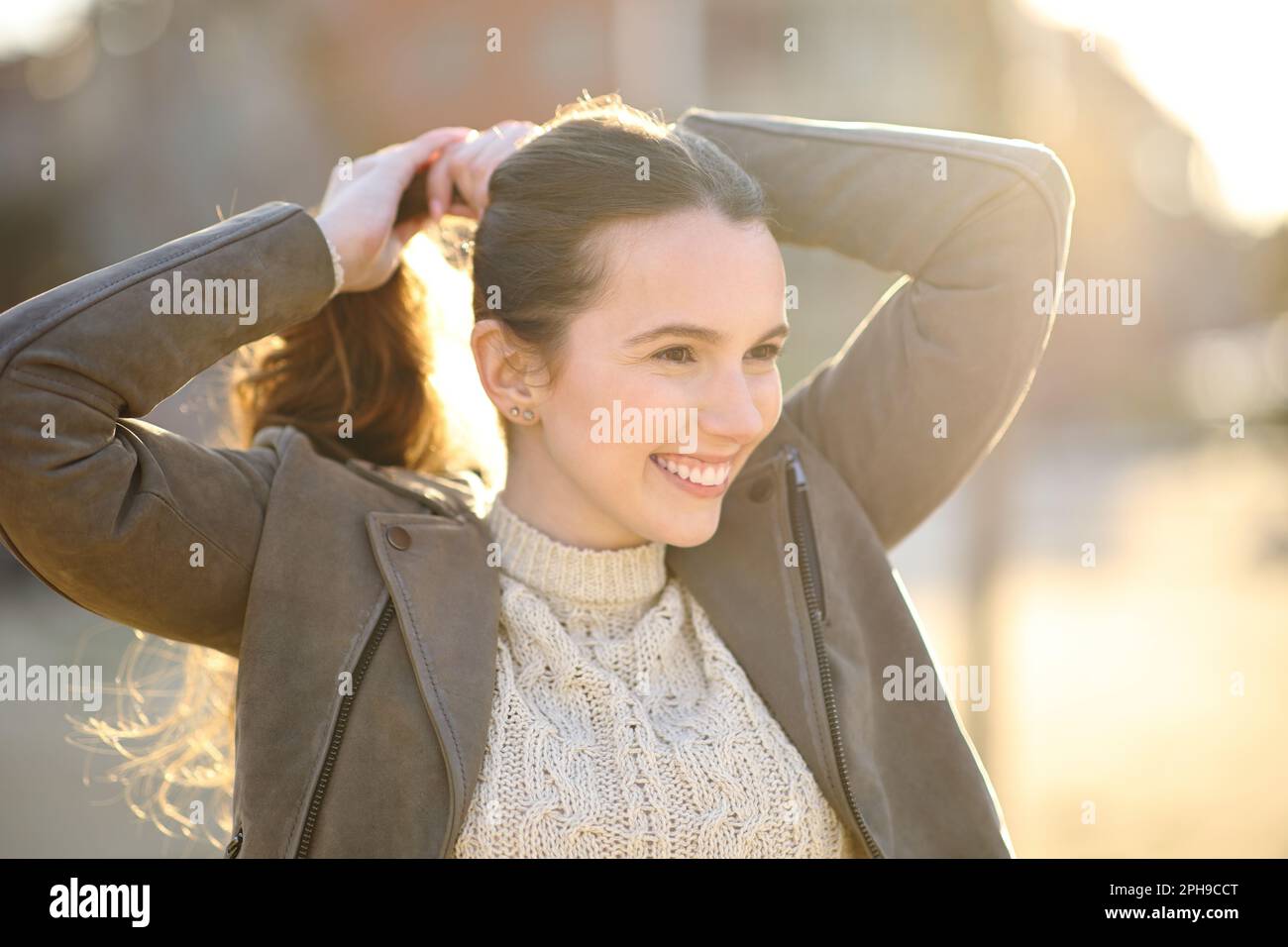 Glückliche Frau, die bei Sonnenuntergang auf der Straße Pferdeschwanz macht Stockfoto