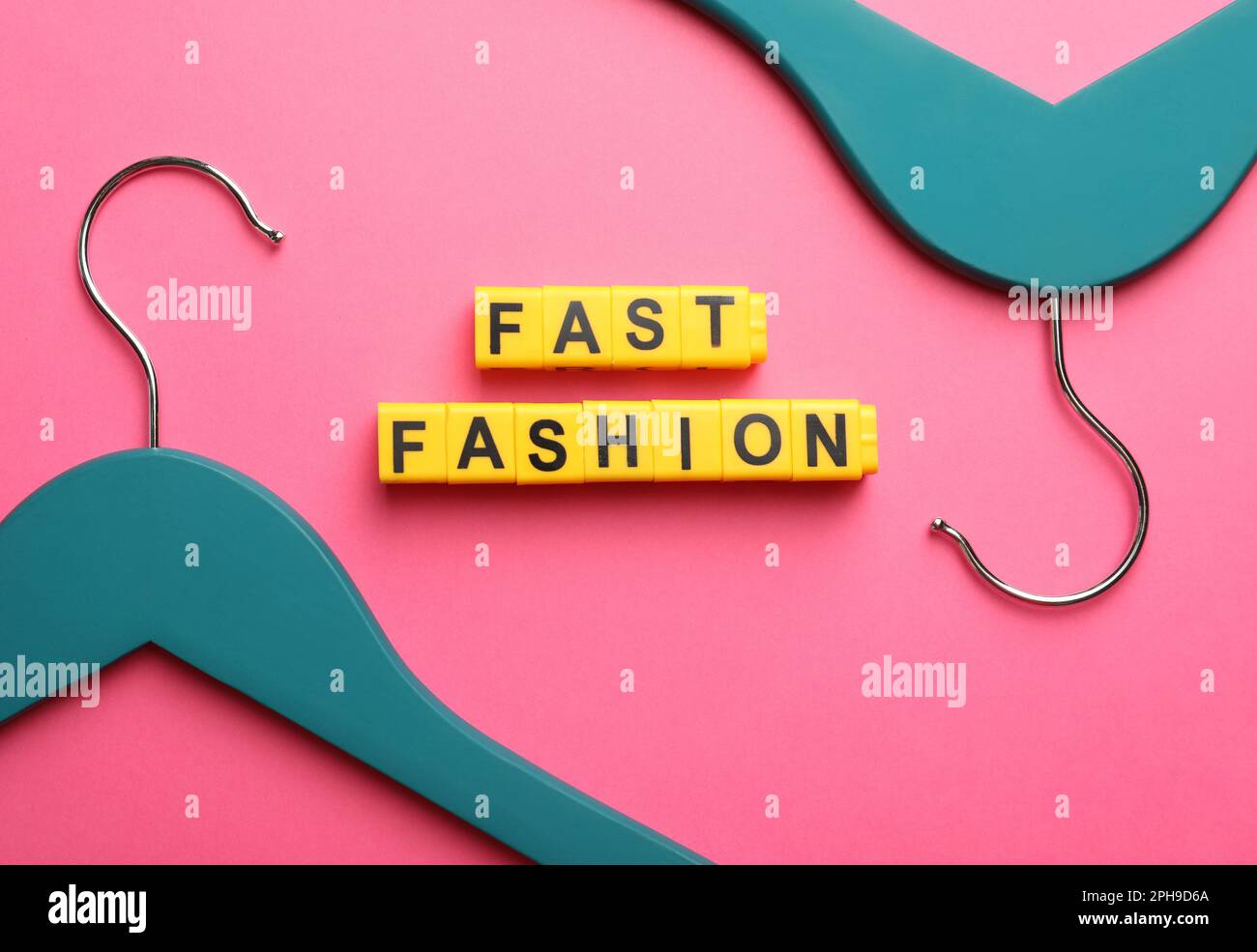 Gelbe Kunststoffwürfel mit der Phrase „Fast Fashion“ und Kleiderbügeln auf pinkfarbenem Hintergrund, flach liegend Stockfoto
