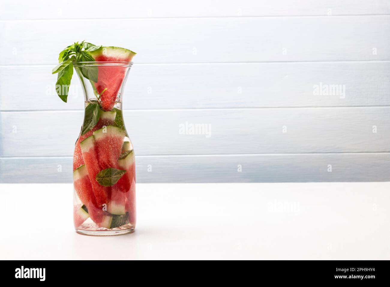Scheiben Wassermelone und ein Zweig grünes Basilikum in einer Karaffe Wasser. Speicherplatz kopieren. Weißer Hintergrund. Stockfoto