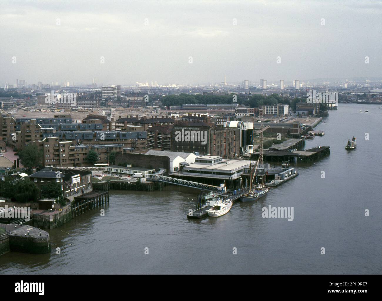 Nach London. 1984. Blick nach Osten vom oberen Fußweg der Tower Bridge über die Themse in London, England. Das Foto zeigt Wapping, wie es vor der umfassenden Sanierung durch die London Docklands Development Corporation war. Im Vordergrund sehen Sie die British & Foreign Wharf und HMS President, eine Einrichtung des Royal Naval Reserve. Stockfoto
