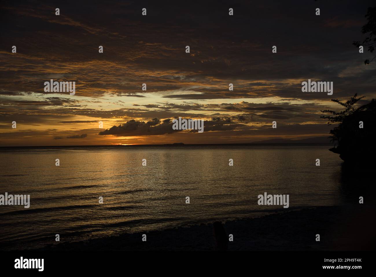 Malerischer Sonnenuntergang am Strand von Siquijor auf den Philippinen, der ganze Himmel leuchtet goldgelb. Stockfoto