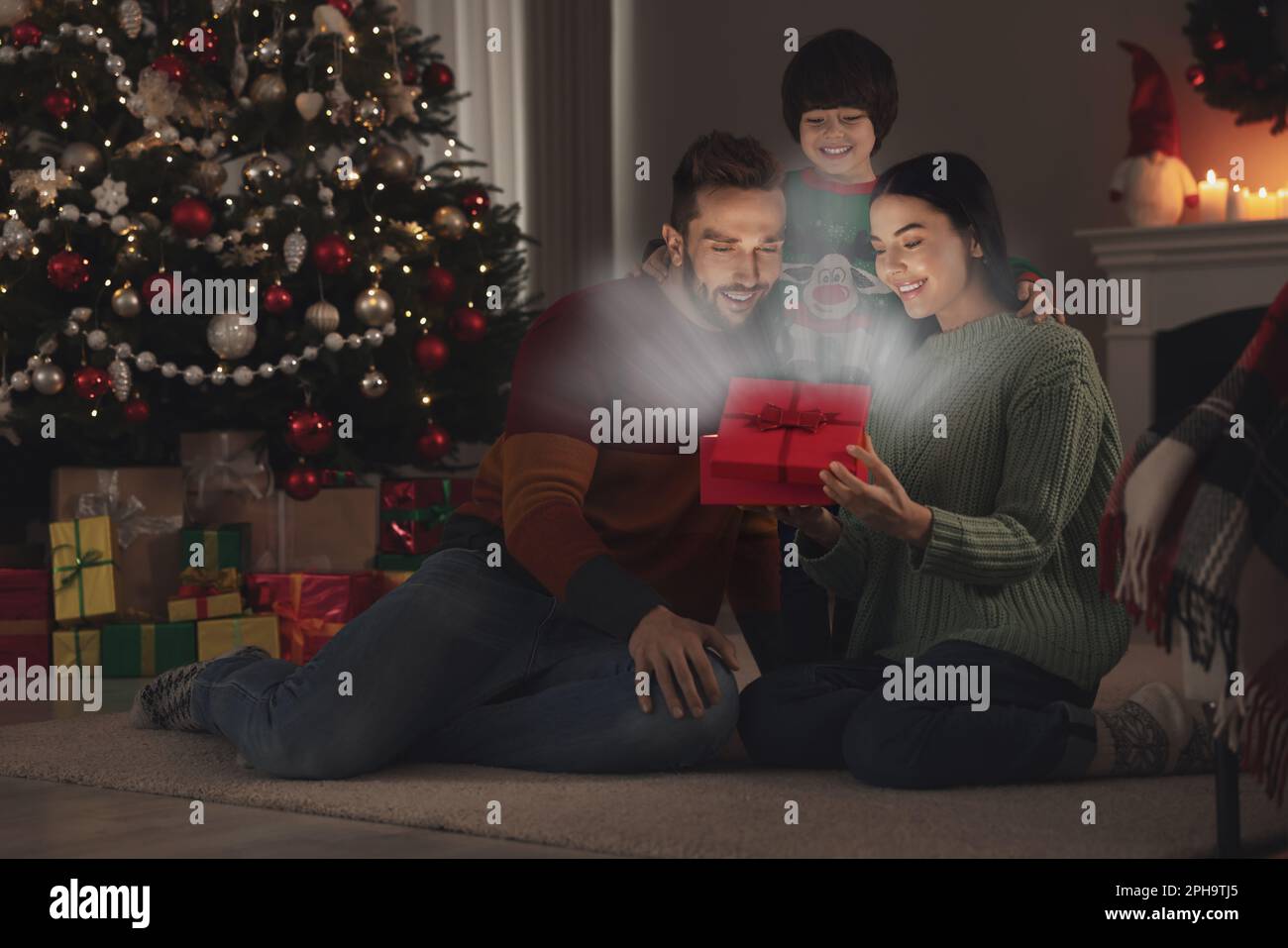 Glückliche Familie eröffnete Geschenkbox mit magischem Licht zu Hause. Weihnachtsfeier Stockfoto