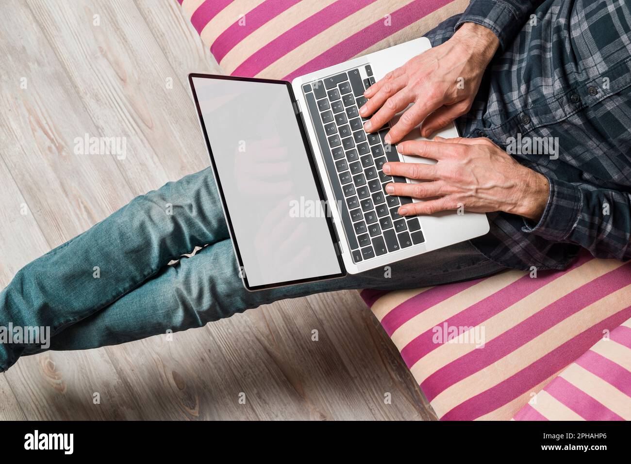 Großer Blickwinkel auf einen Mann, der einen Laptop mit leerem Bildschirm benutzt, der auf dem Sofa sitzt. Stockfoto