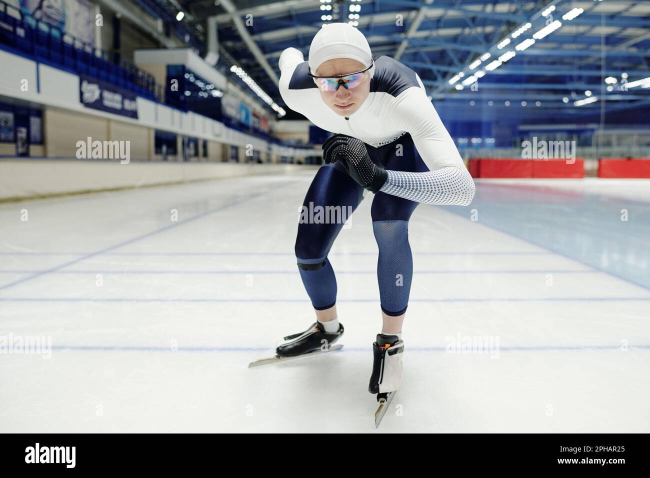 Junger Sportler in Uniform und Brille, der an der Startlinie auf Skates steht und sich während eines kurzen Speed Skating-Rennens vorwärts bewegt Stockfoto