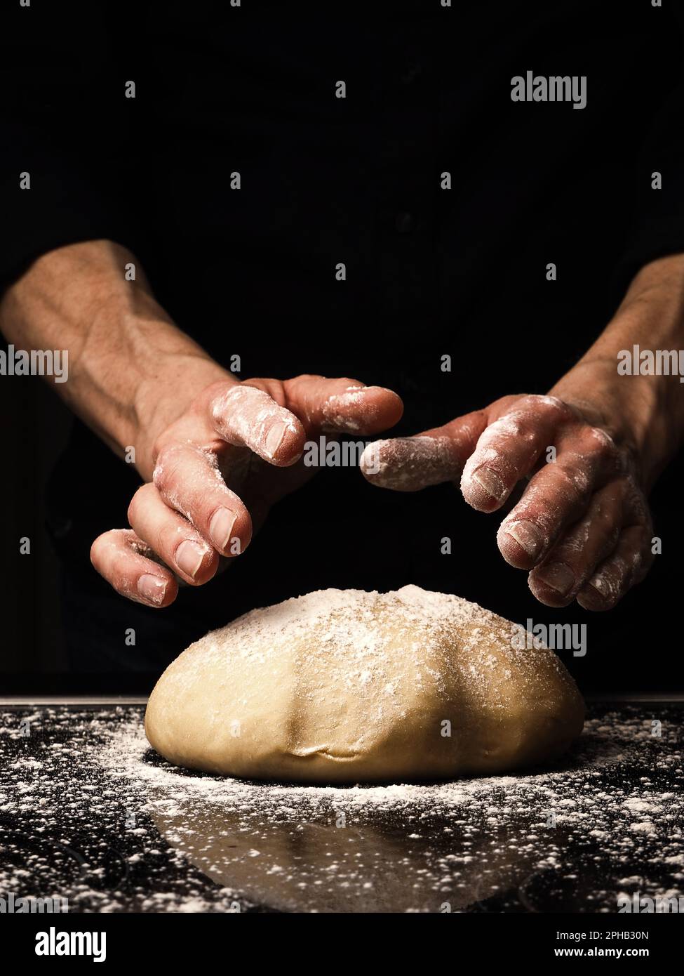 Bäcker oder Koch kneten einen Bio-Hefeteig, schwarzer Hintergrund mit Platz für Ihren Text oder Ihr Bild, traditionelle Handarbeit in der Küche Stockfoto