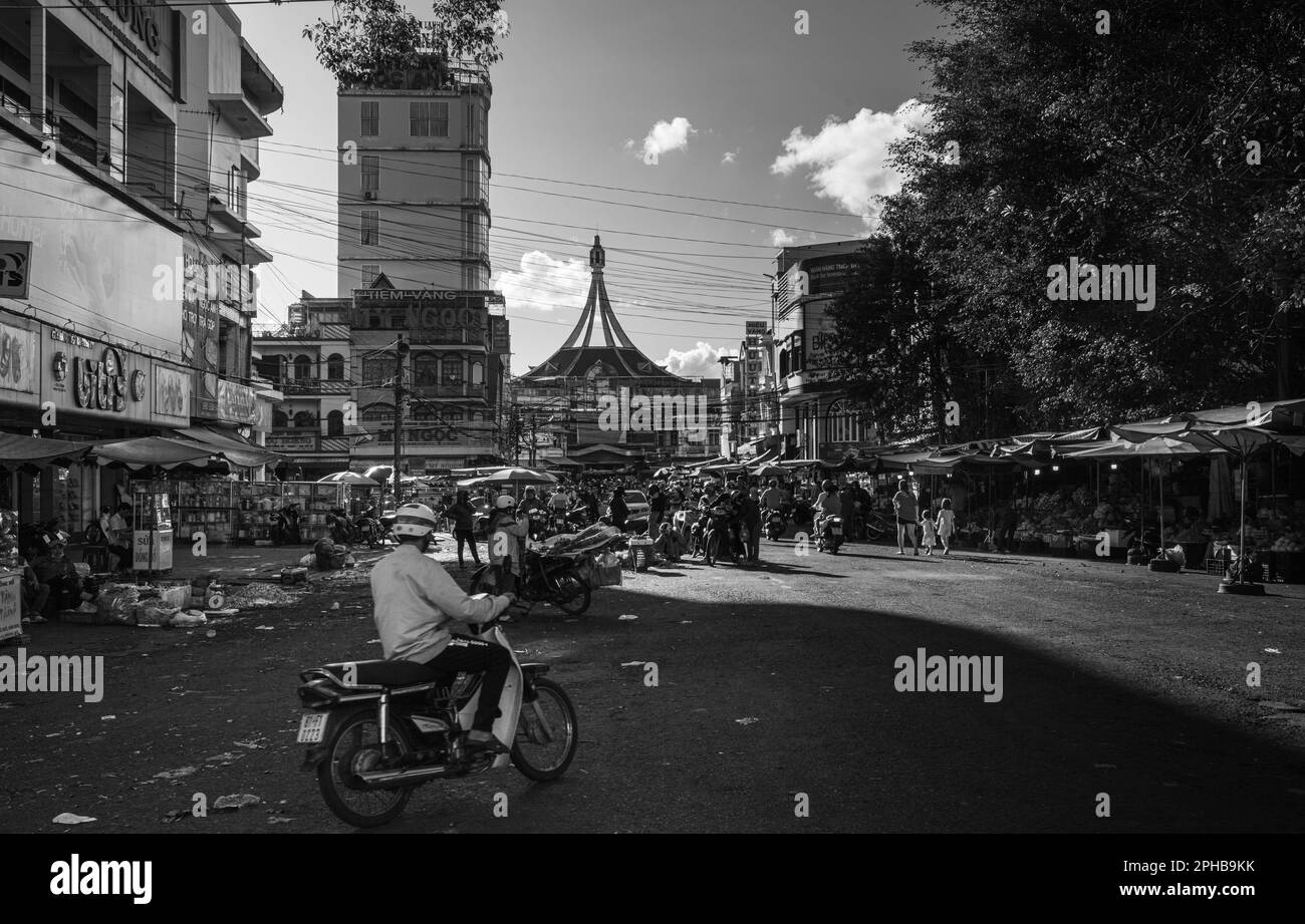 Ein Mann fährt mit dem Motorrad in Richtung der überfüllten Straßen vor dem Wahrzeichen Central Market in Pleiku im zentralen Hochland Vietnams. Stockfoto