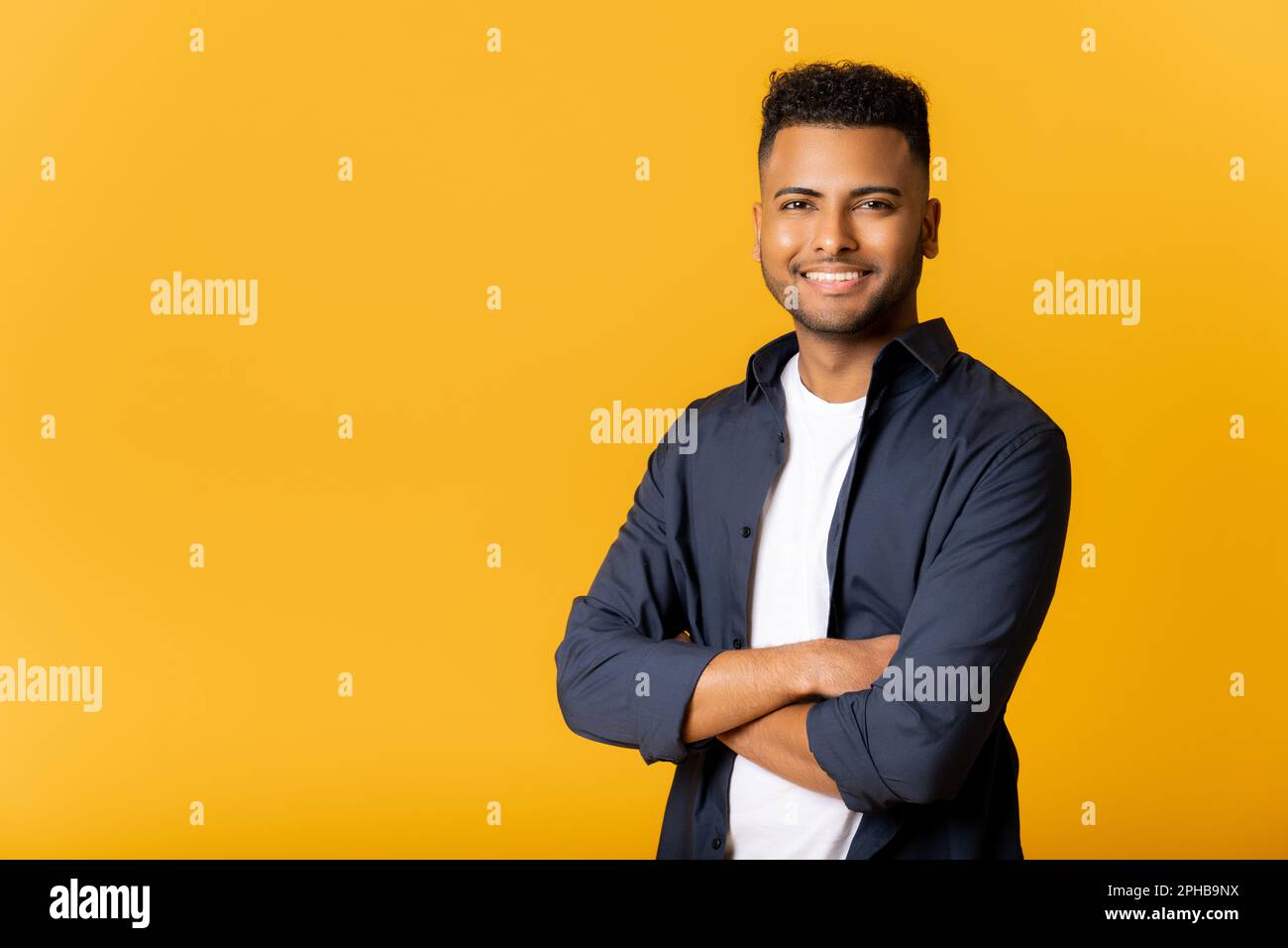 Selbstbewusster junger indischer Mann, der selbstbewusst in einer selbstbewussten Pose steht, mit verschränkten Armen in die Kamera schaut, Kopierraum für Werbung für neue Werbung, arabischer Kerl, der isoliert auf gelbem Hintergrund steht. Stockfoto