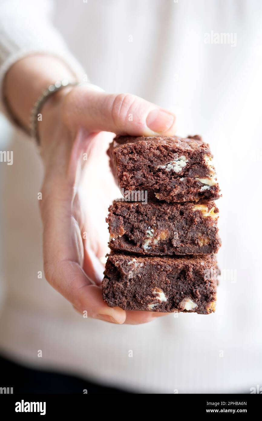 Eine Frau mit drei gestapelten, frisch gebackenen, dreifachen Schokoladenbrownies. Die Brownies sind frisch und lecker. Ein Genuss Stockfoto