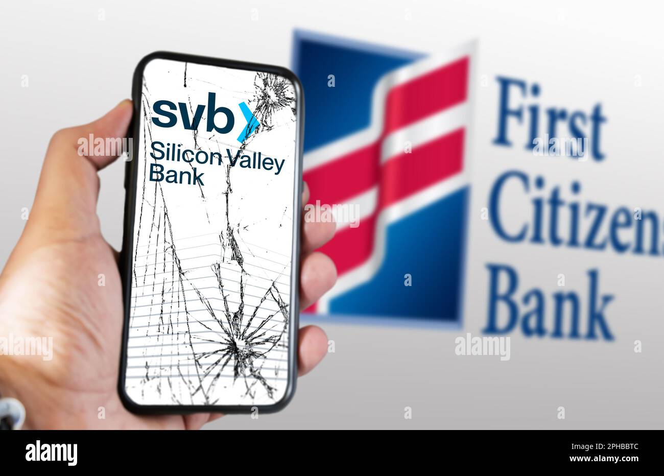 New York, USA, März 2023: Hand hält ein Telefon mit Silicon Valley Bank Logo auf einem rissigen Bildschirm. Logo der First Citizens Bank auf weißem Hintergrund verschwommen. Stockfoto