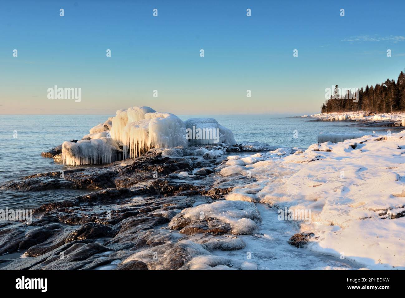 Eis überzieht ein felsiges Seeufer unter azurblauem Himmel Stockfoto