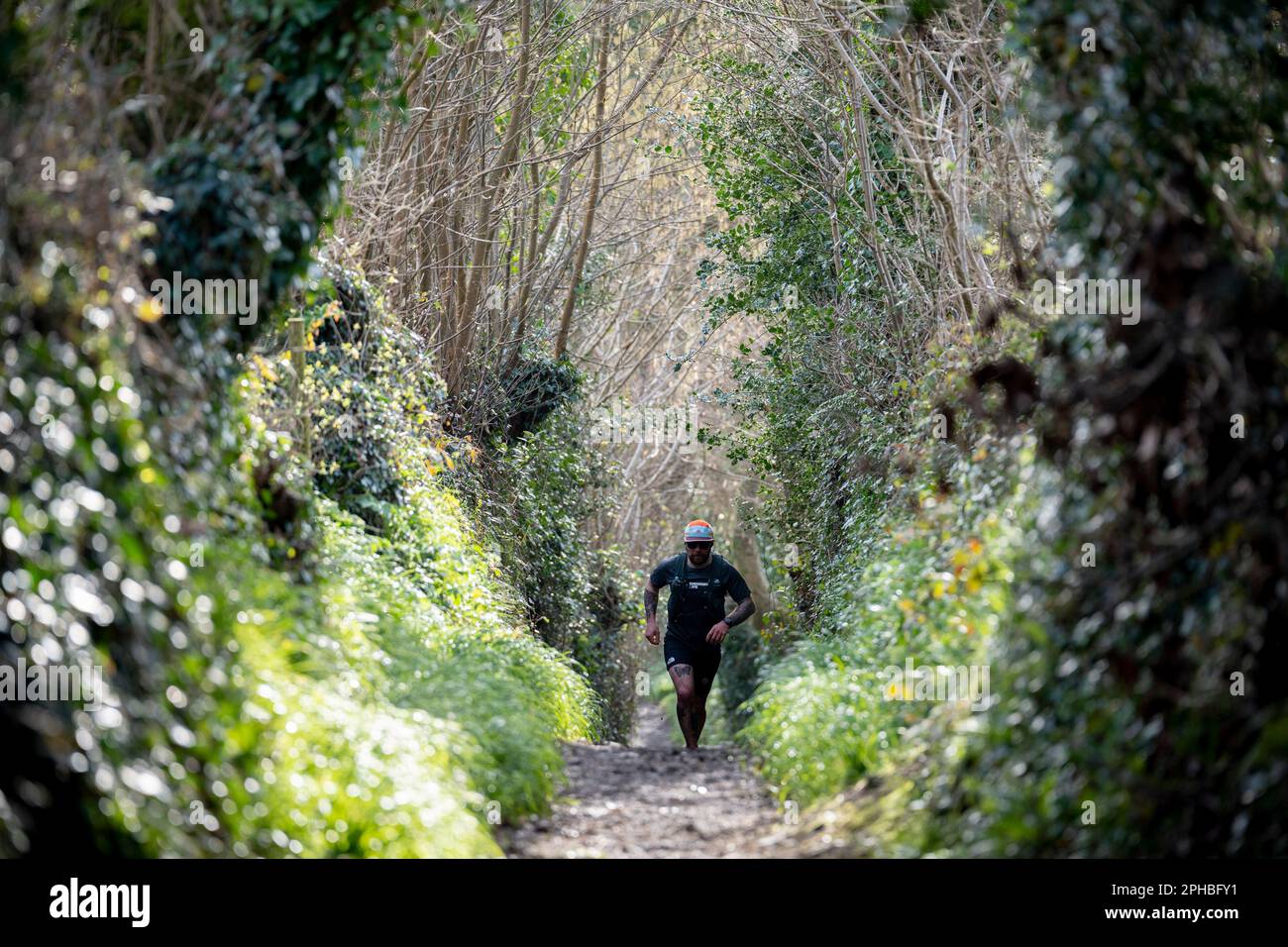 Ein Mann läuft am 19. März 2023 in Mawnan Smith in Cornwall, England, über eine schlammige ländliche Strecke in die Ferne. Stockfoto