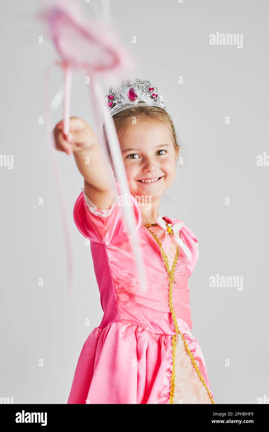 Ein kleines Mädchen, das ihre Rolle als Prinzessin genießt. Ein bezauberndes, niedliches 5-6-jähriges Mädchen, das ein pinkfarbenes Prinzessinnen-Kleid und Diadem trägt und magische Zauberstab-Standdi verwendet Stockfoto