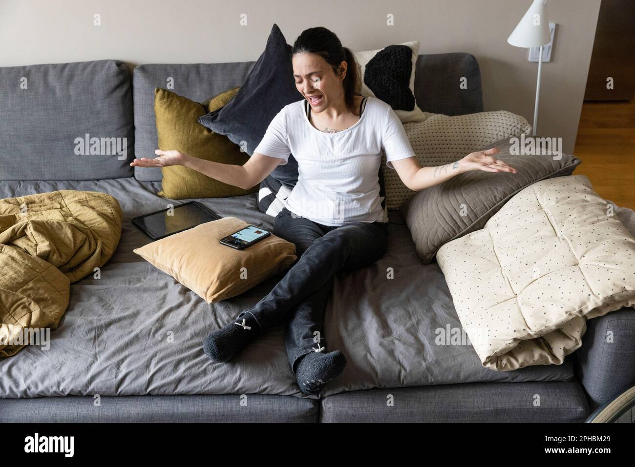 Frau mit Behinderungsgesten, während sie auf dem Sofa auf ein Smartphone schaut Stockfoto