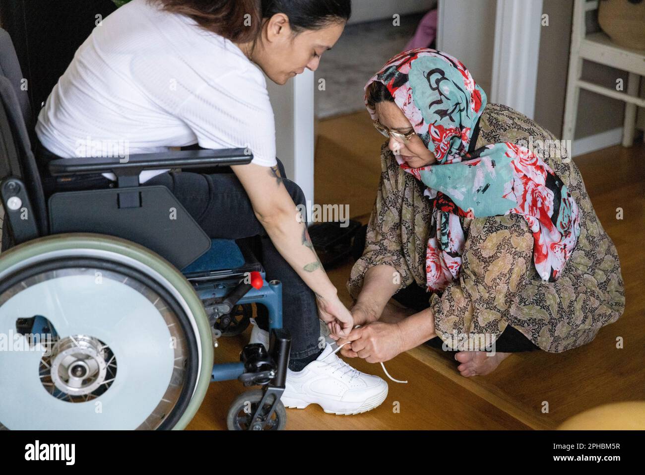 Mutter bindet den Schnürsenkel einer Tochter, die zu Hause im Rollstuhl sitzt Stockfoto