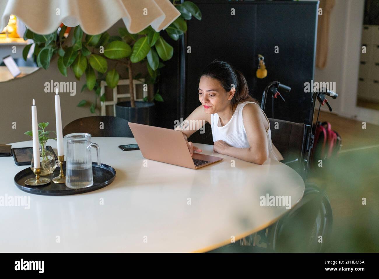 Frau mit Behinderung, die zu Hause einen Laptop auf dem Esstisch benutzt Stockfoto