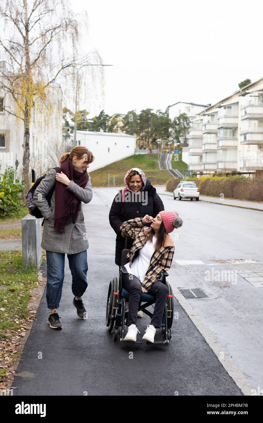 Mutter und Krankenschwester reden mit einer Frau, die auf einem Rollstuhl sitzt und auf dem Bürgersteig läuft Stockfoto
