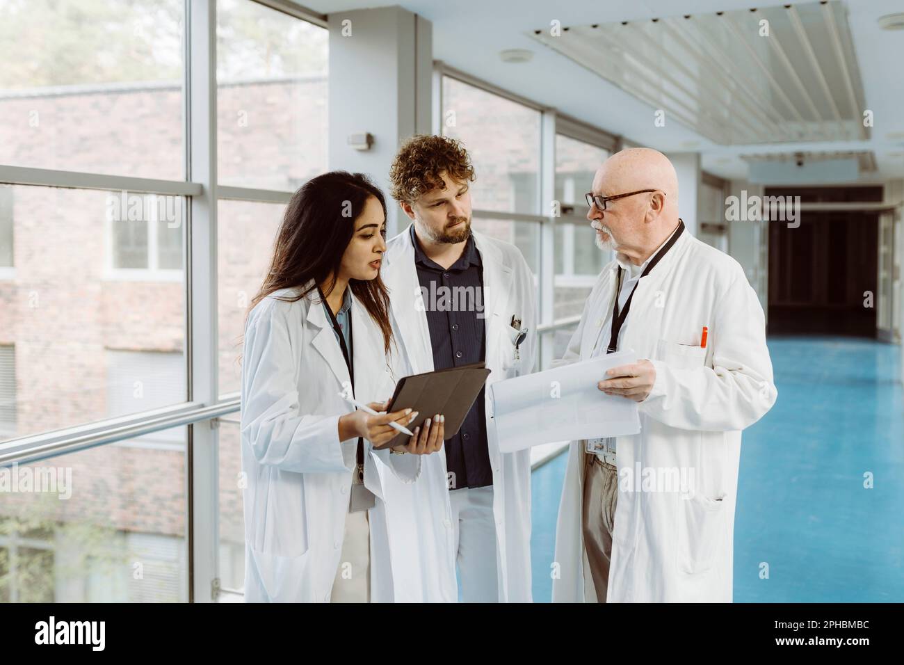 Kollegen aus dem Gesundheitswesen diskutieren über ein digitales Tablet und dokumentieren, während sie gemeinsam im Krankenhausflur stehen Stockfoto Kollegen aus dem Gesundheitswesen diskutieren über ein digitales Tablet und dokumentieren, während sie gemeinsam im Krankenhausflur stehen Stockfoto