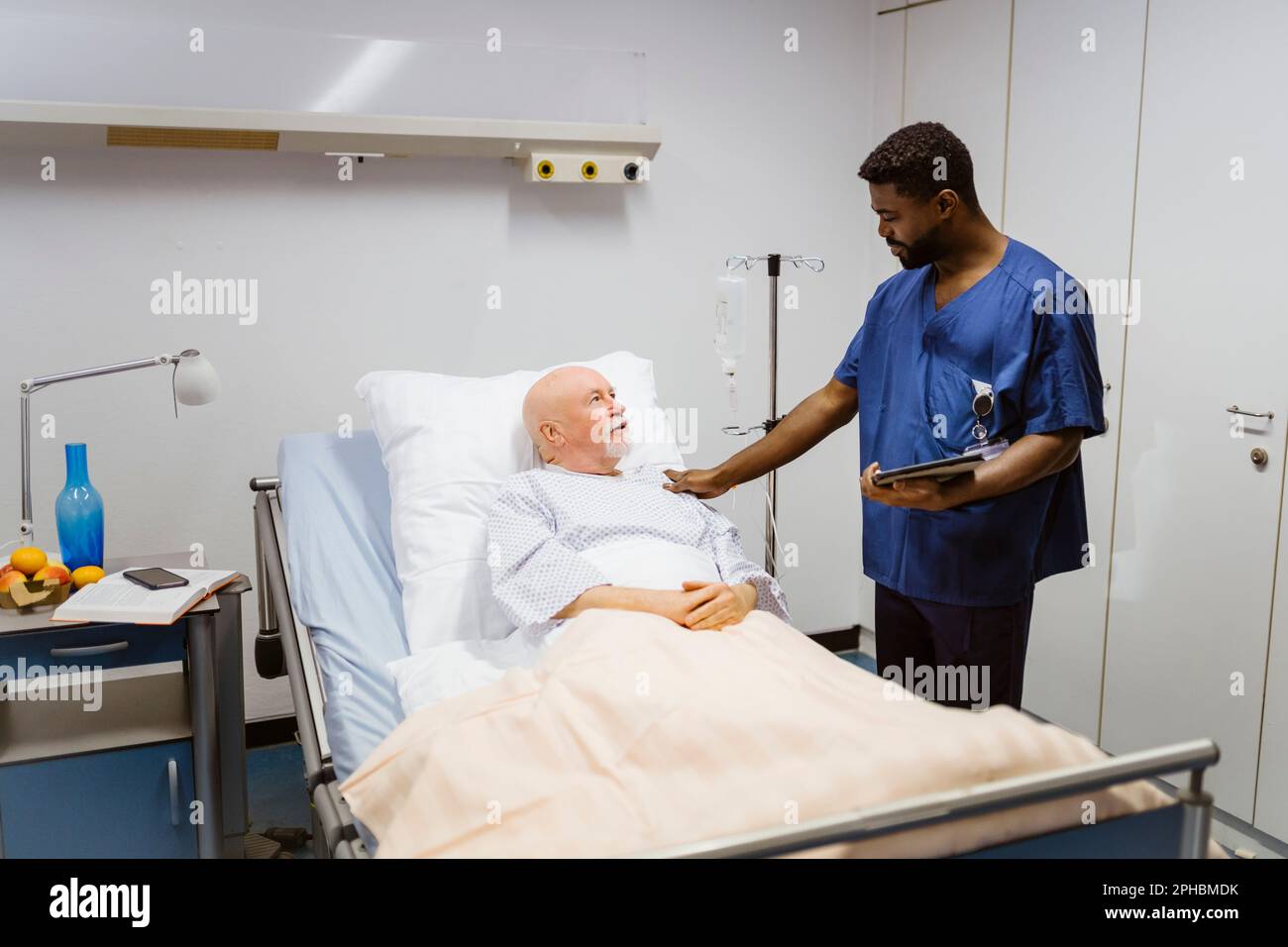 Krankenschwester mit Hand auf Schulter des im Krankenhaus liegenden Seniorpatienten Stockfoto