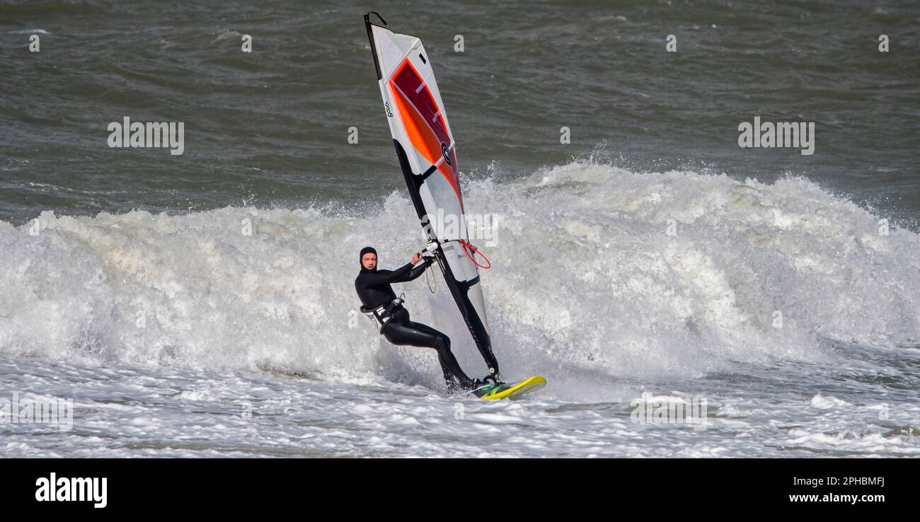 Windsurfer in schwarzem Neoprenanzug, der bei Wind und Wintersturm an der Nordseeküste klassisches Windsurfen praktiziert Stockfoto