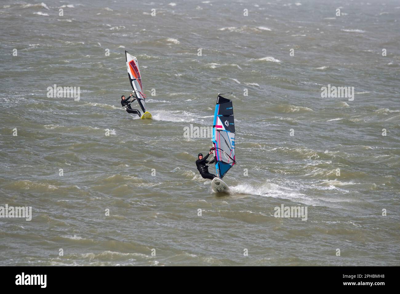Zwei Windsurfer in schwarzen Neoprenanzügen üben klassisches Windsurfen an der Nordseeküste bei Wind und Wintersturm Stockfoto