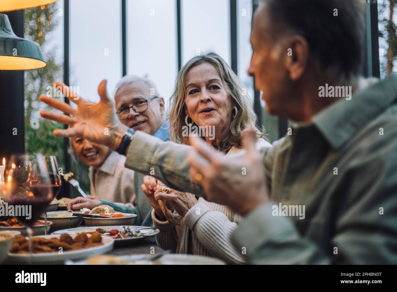 Seniorin hört männlichen Freunden zu, während sie auf der Dinnerparty spricht Stockfoto