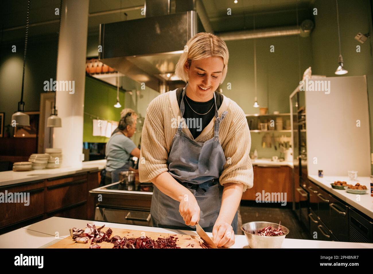 Lächelnde nicht-binäre Person, die Gemüse während des Kochkurses in der Küche zerkleinert Stockfoto