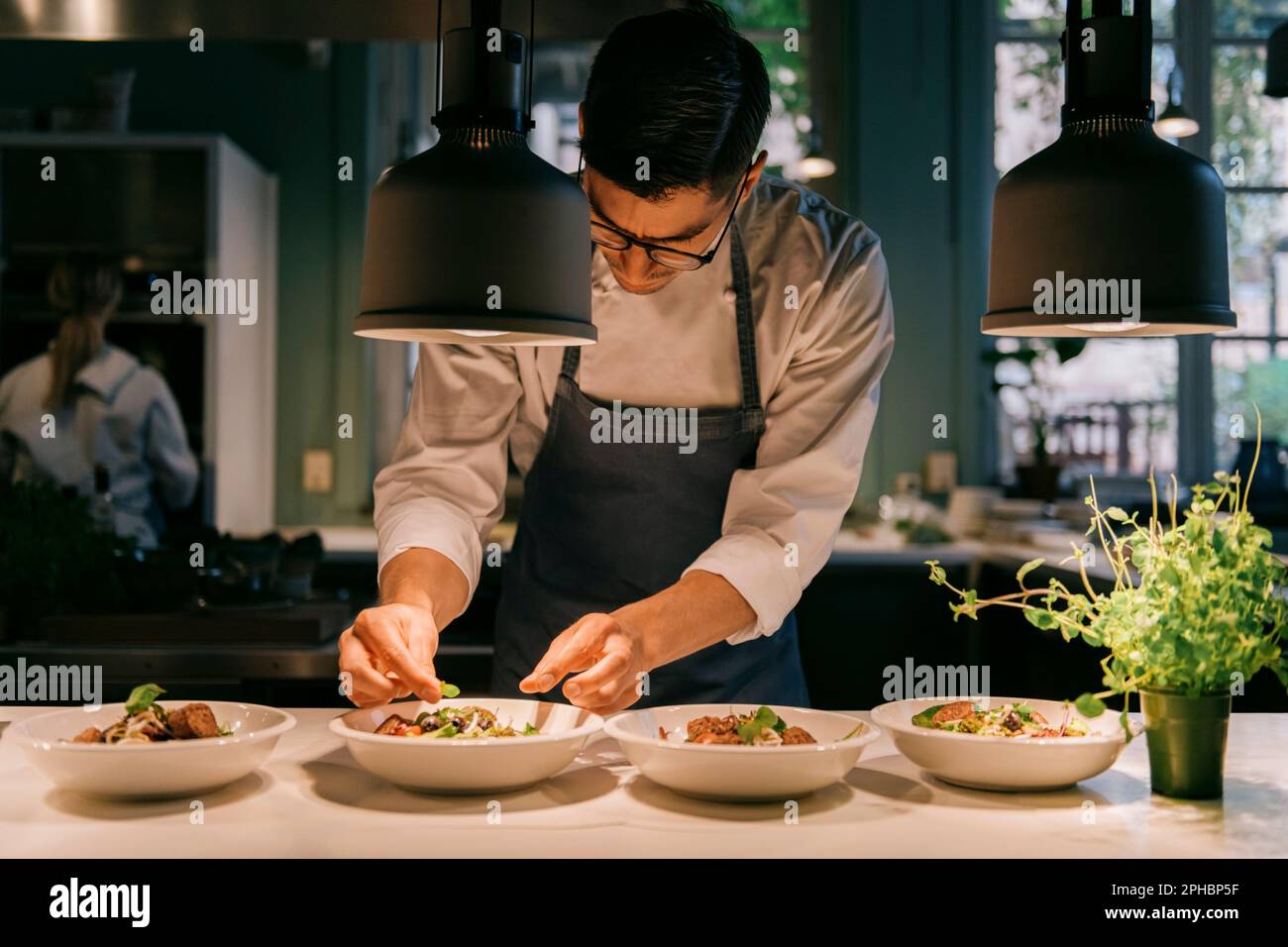 Männlicher Koch garniert Essen mit Kräutern unter Licht in der kommerziellen Küche Stockfoto