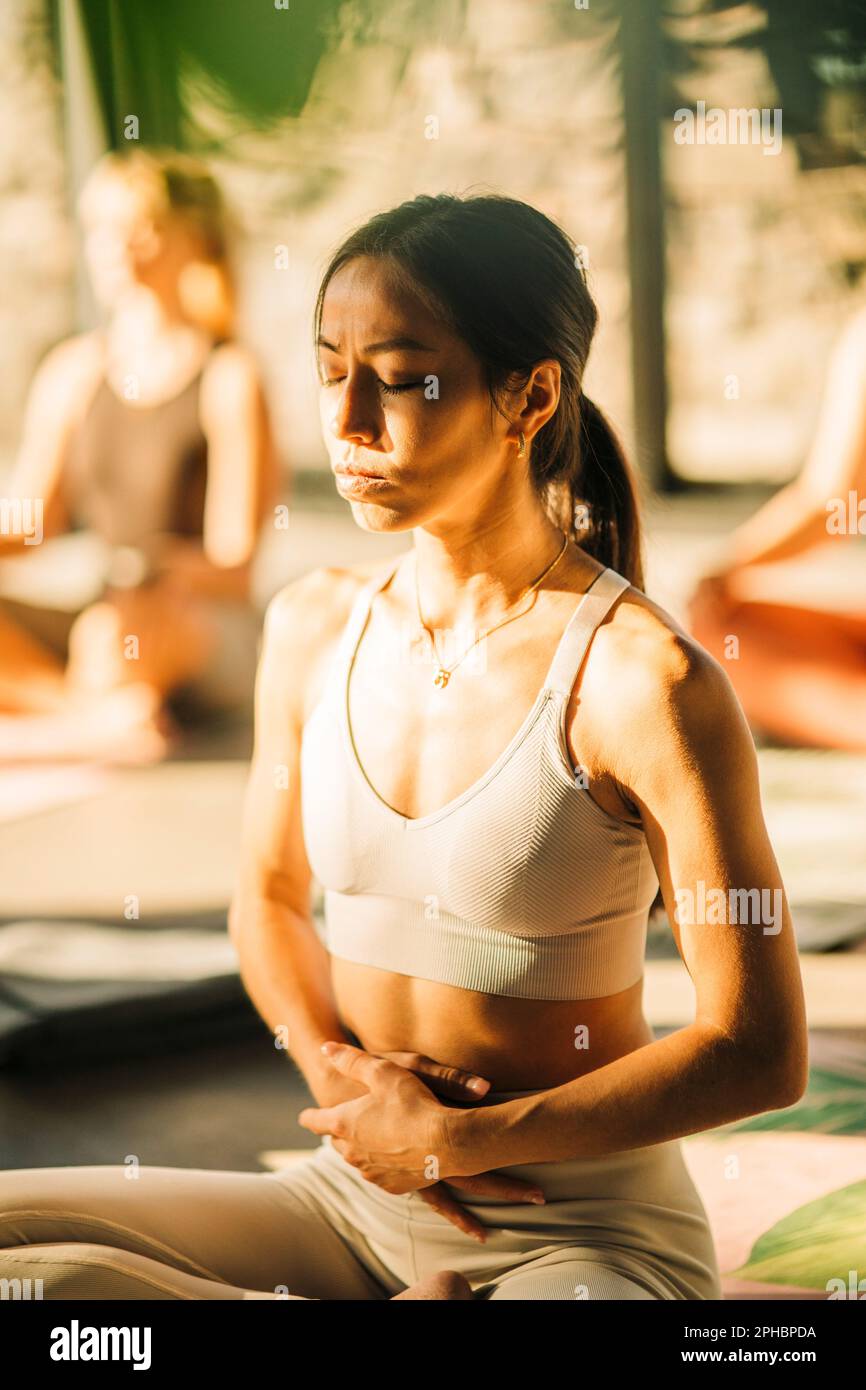 Junge Frau mit den Händen am Magen, die Yoga im Rückzugszentrum praktiziert Stockfoto