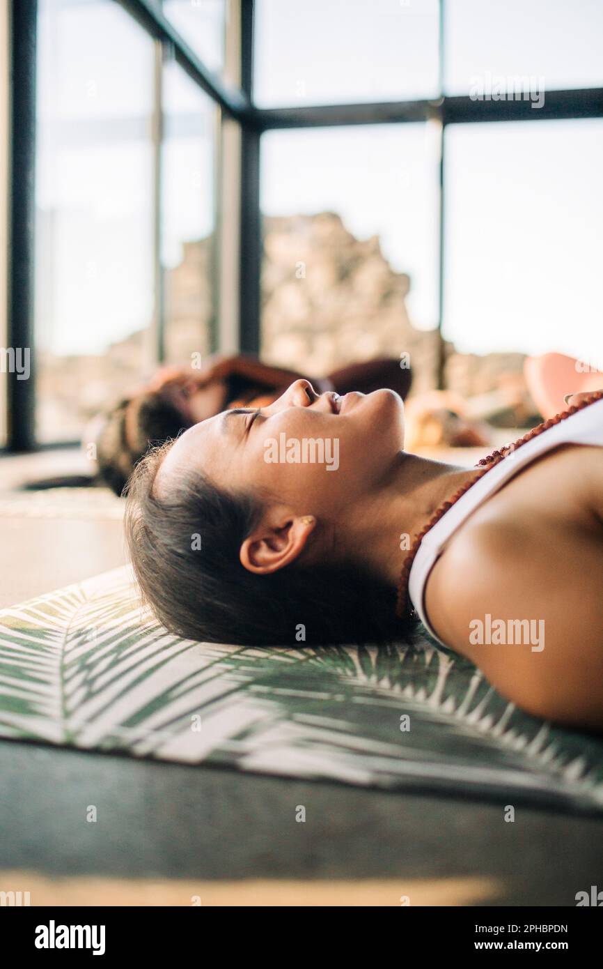 Lächelnde Lehrerin, die auf der Trainingsmatte liegt, während sie Yoga im Rückzugszentrum macht Stockfoto