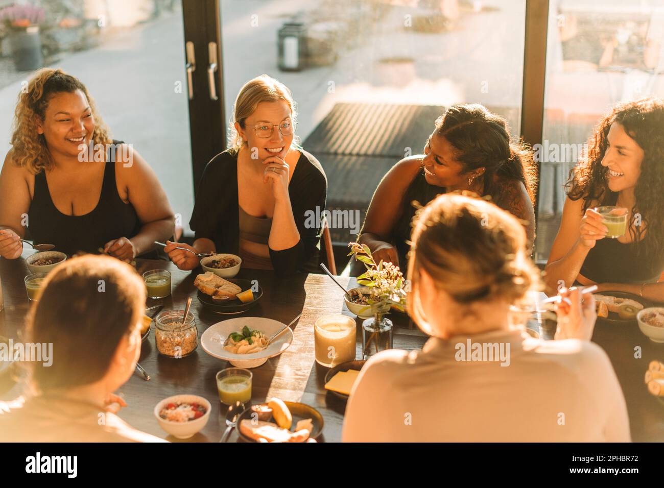 Eine Frau mit Hand am Kinn, die während des Frühstücks mit weiblichen Freunden im Rückzugszentrum spricht Stockfoto