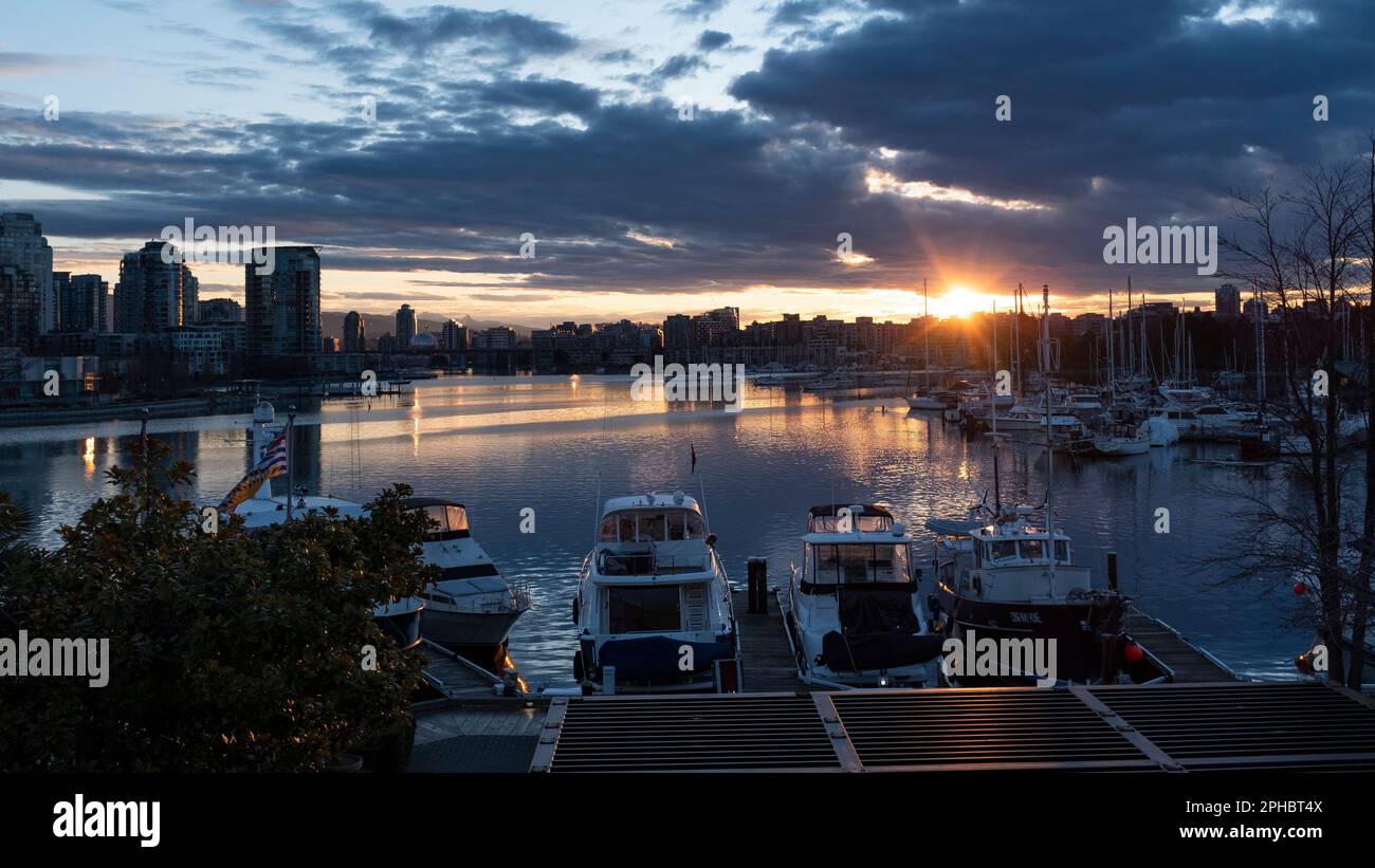 Sonnenaufgang über False Creek, mit Booten im ruhigen Wasser nahe Granville Island und der Skyline von Vancouver, British Columbia in der Ferne. Stockfoto