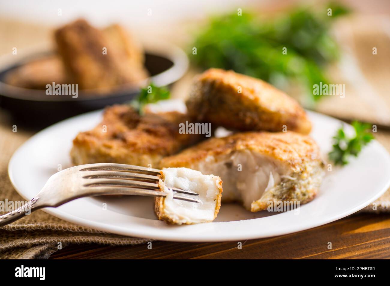 Ein Stück Seehecht, gebraten in knuspriger Kruste, auf einem Teller auf einem Holztisch. Stockfoto