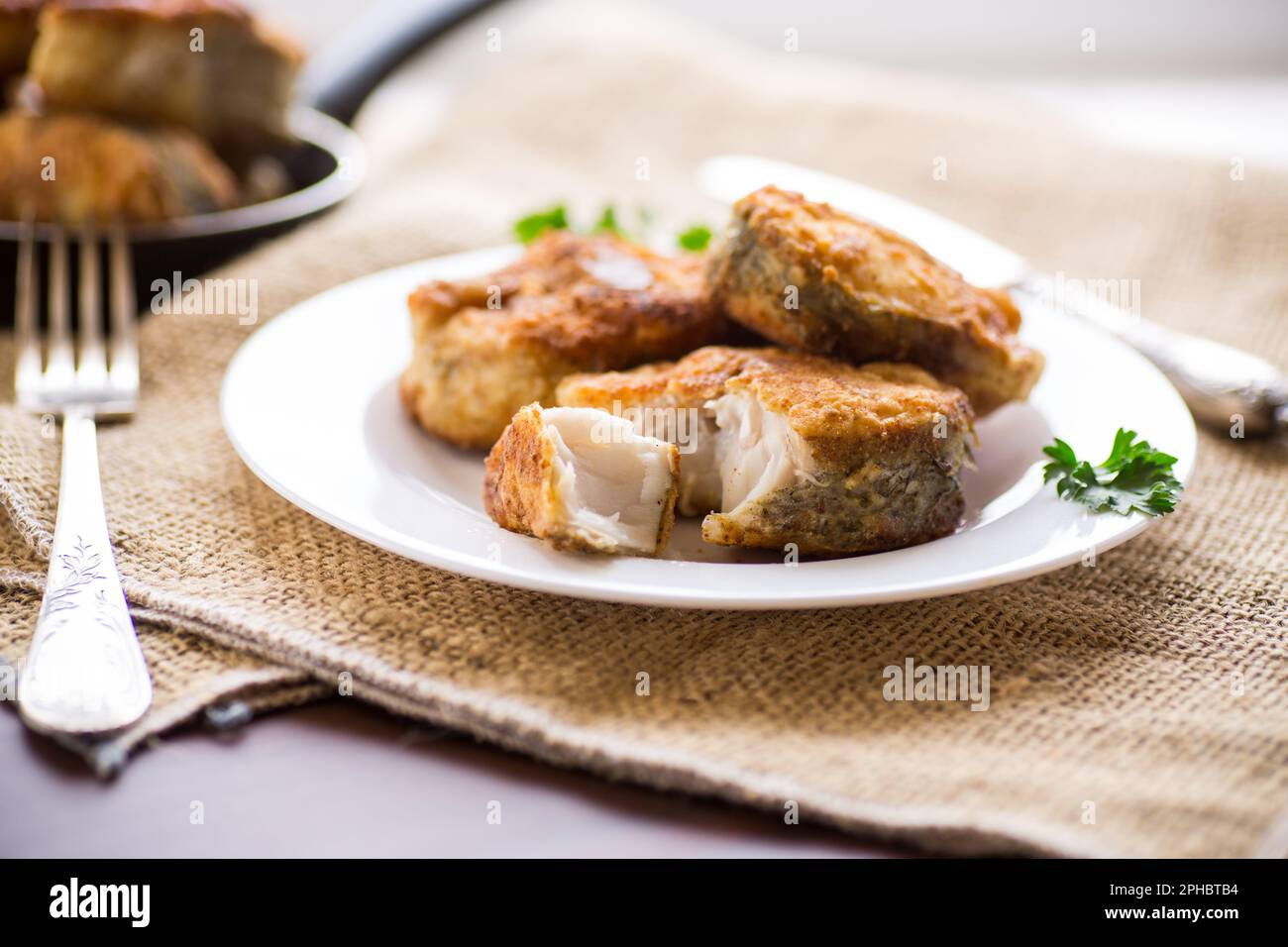 Ein Stück Seehecht, gebraten in knuspriger Kruste, auf einem Teller auf einem Holztisch. Stockfoto
