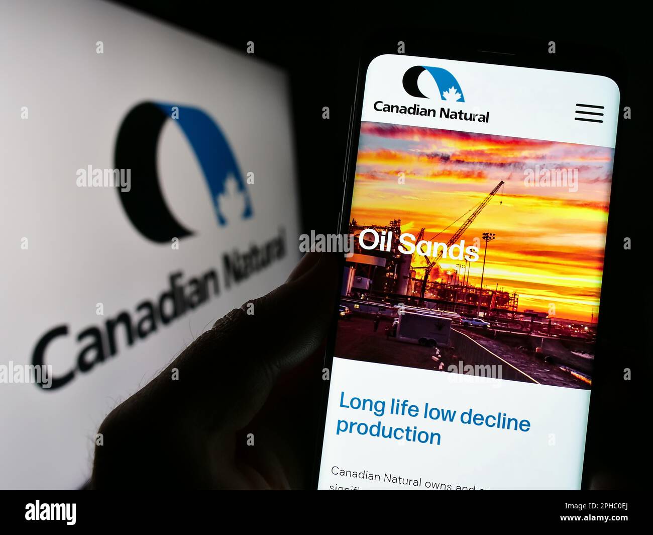 Person mit Smartphone und Webseite des Unternehmens Canadian Natural Resources Limited auf dem Bildschirm vor dem Logo. Konzentrieren Sie sich auf die Mitte des Telefondisplays. Stockfoto
