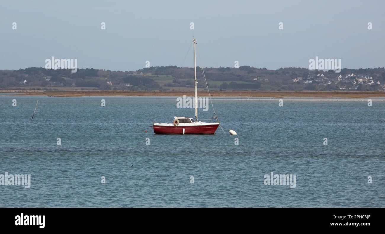 Ein rotes Segelboot ist in einer Bucht vor Anker, das Wasser bewegt sich nicht, die weiße Boje vor dem Laderaum ist an Ort und Stelle. Stockfoto