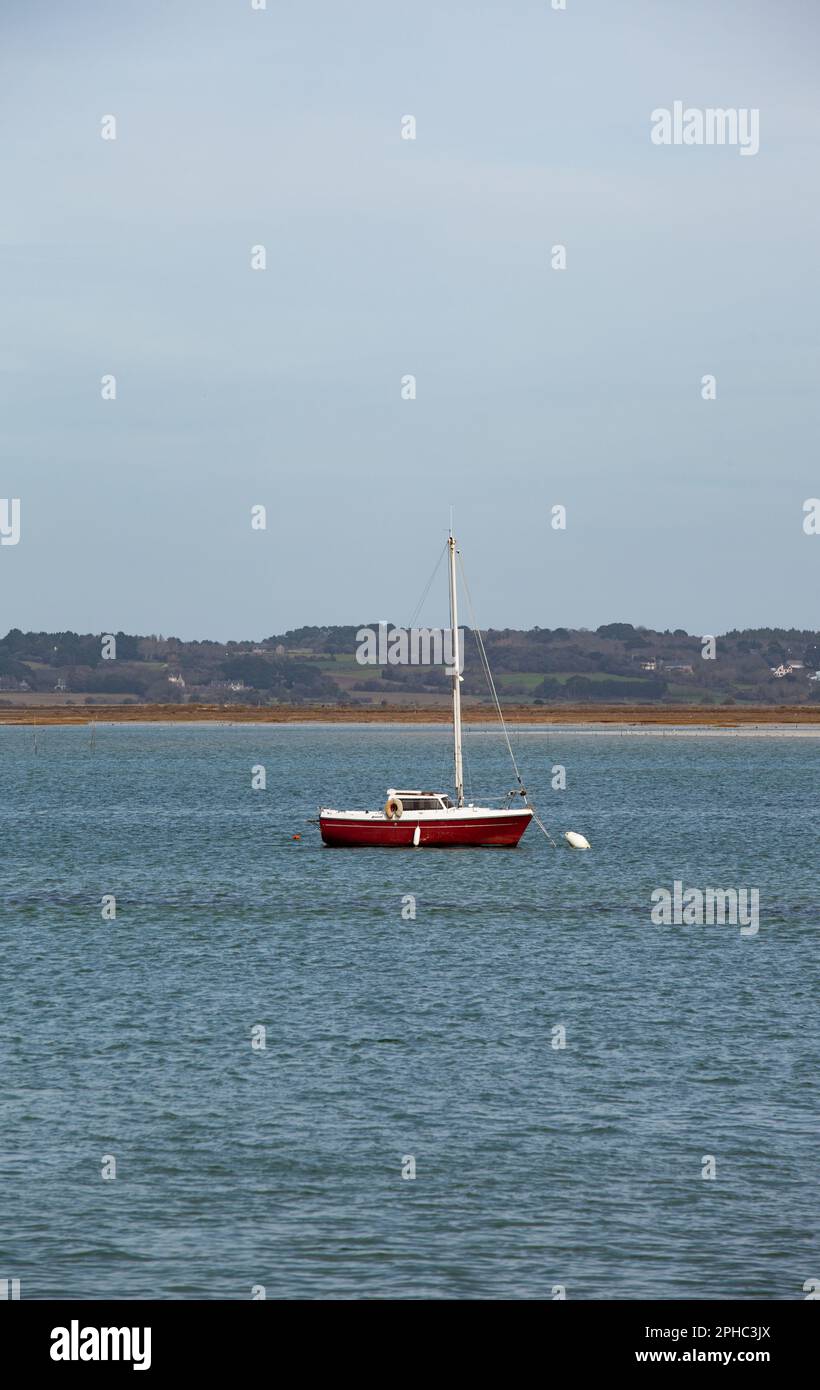 Ein rotes Segelboot ist in einer Bucht vor Anker, das Wasser bewegt sich nicht, die weiße Boje vor dem Laderaum ist an Ort und Stelle. Stockfoto