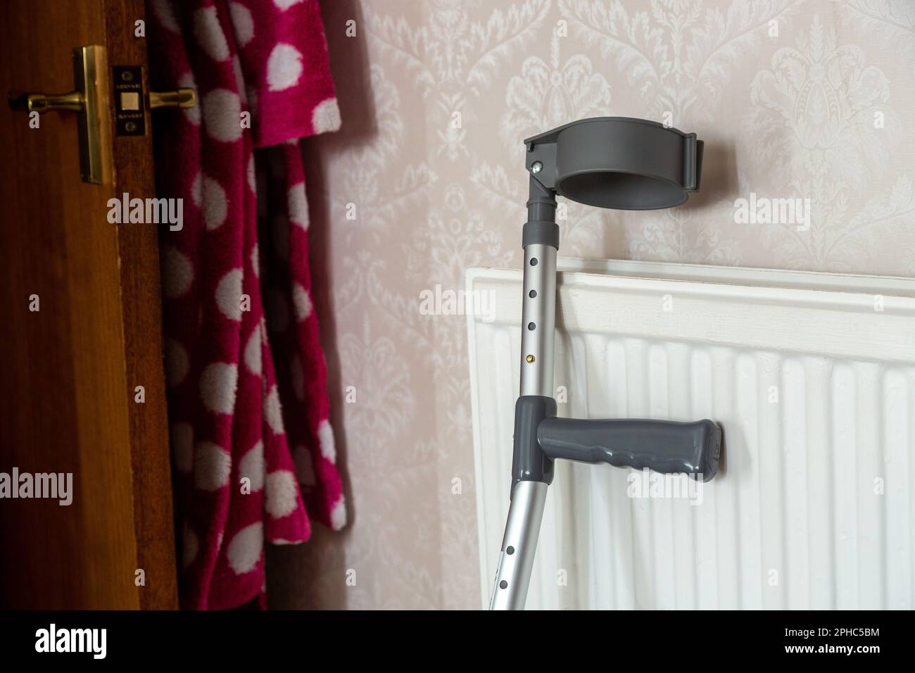 Eine Krücke, die sich gegen eine Heizung in einem Schlafzimmer lehnt Stockfoto