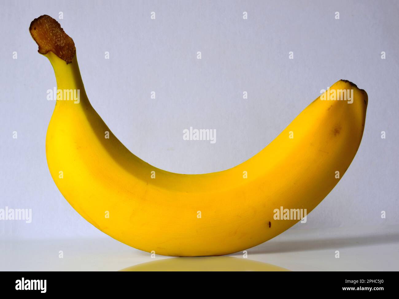 Isolierte einreife gelbe Banane auf weißer Oberfläche und weißem Hintergrund. Reflexion und Schatten. Abstraktes Bild. Stillleben und Kunst. Organisch und gesund Stockfoto