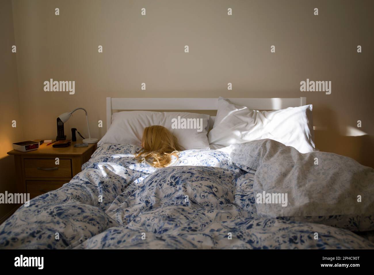 Eine blonde Frau (Schaufensterpuppe), die im Bett schläft und von Morgensonne beleuchtet wird Stockfoto