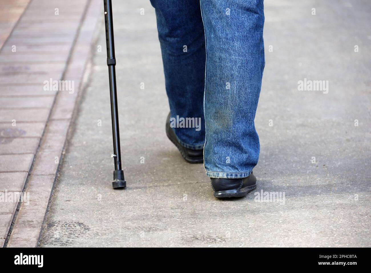 Ein Mann in Jeans, der mit einem Stock auf einer Straße läuft, Beine auf dem Bürgersteig. Behinderungsbegriff, hinkender Seniorenreisender, Wirbelsäulenerkrankungen Stockfoto