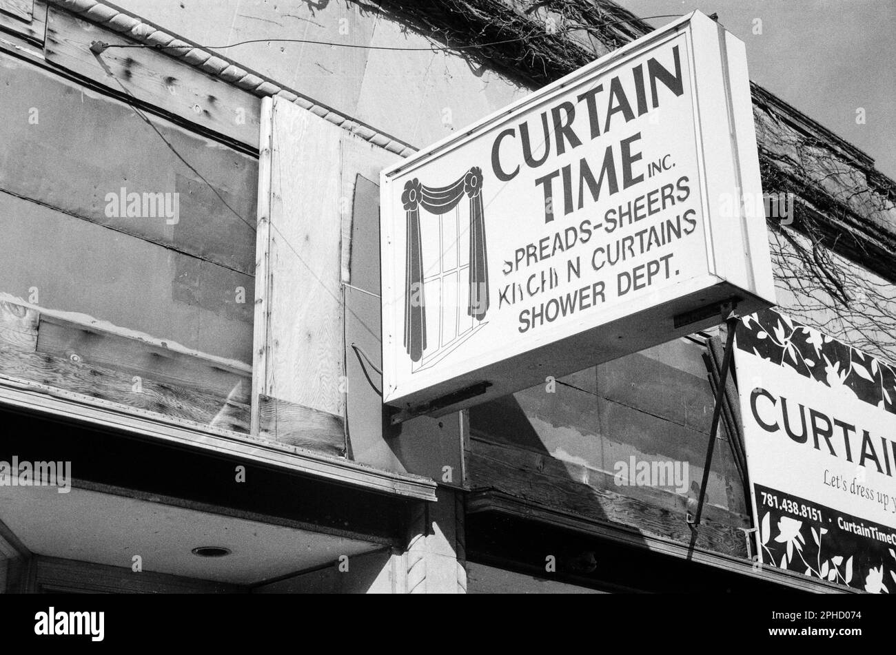 Ein verwittertes Schild mit der Aufschrift „Curtain Time Inc.“ hängt an einer Holzwand mit alten Weinreben über einem Schaufenster in Stoneham, Massachusetts. Das Bild war Stockfoto