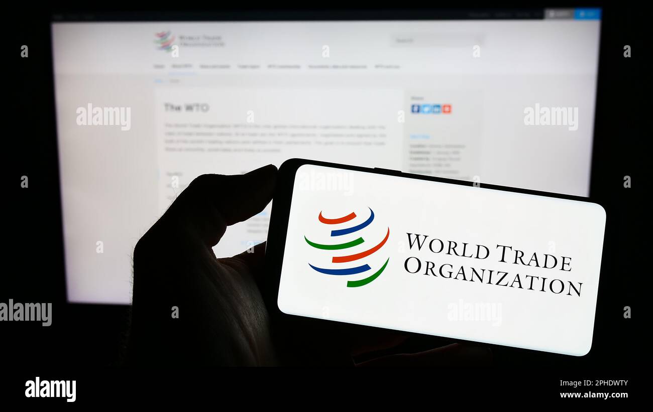 Person, die ein Mobiltelefon mit dem Logo der Welthandelsorganisation (WTO) auf dem Bildschirm vor der Webseite hält. Konzentrieren Sie sich auf das Display des Telefons. Stockfoto Person, die ein Mobiltelefon mit dem Logo der Welthandelsorganisation (WTO) auf dem Bildschirm vor der Webseite hält. Konzentrieren Sie sich auf das Display des Telefons. Stockfoto