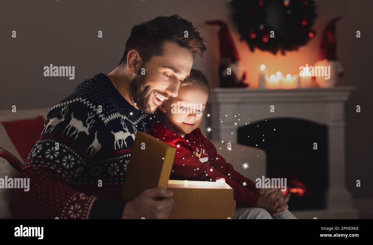 Vater und seine süße Tochter öffnen zu Hause eine Geschenkbox mit magischem Licht. Weihnachtsfeier Stockfoto