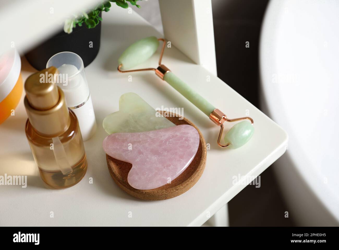 Gua Sha Werkzeuge, Roller mit natürlichem Gesicht und Toilettenartikel auf weißem Regal Stockfoto
