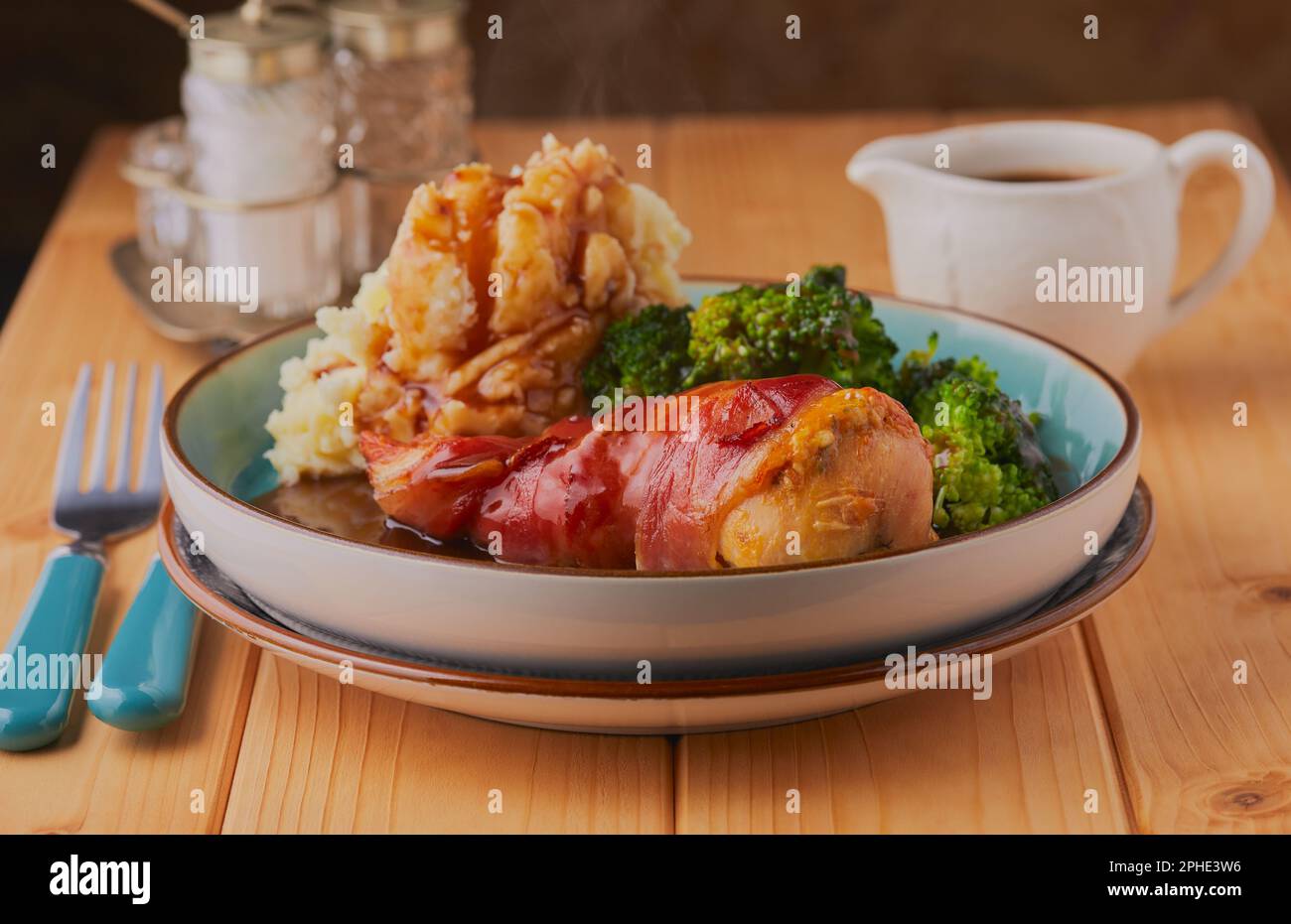 Gefüllte Hähnchenbrust, eingewickelt in Speck, serviert mit Kartoffelpüree und Brokkoli mit Bratensoße. Stockfoto