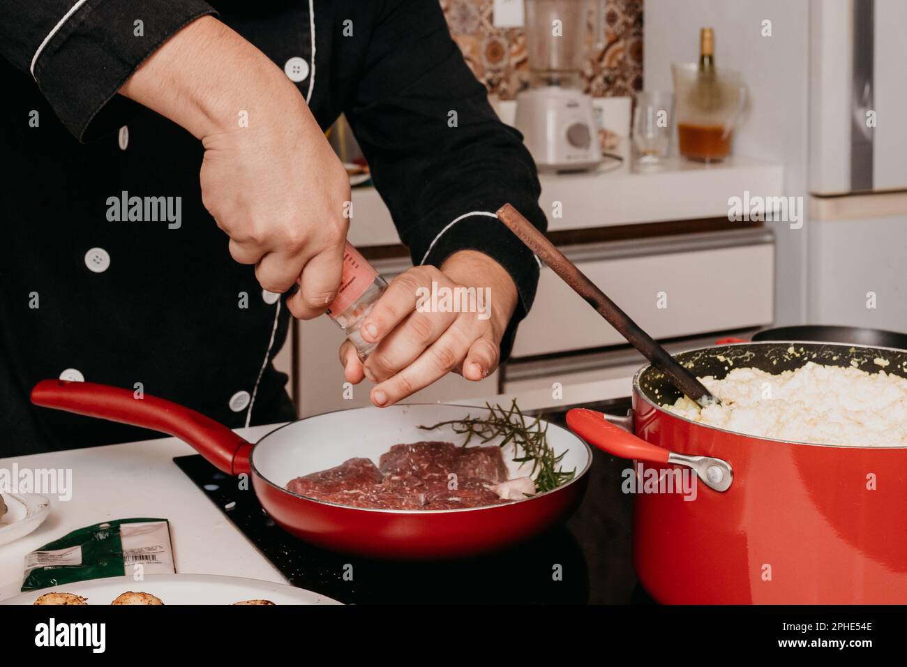 Ein professioneller Koch bereitet sorgfältig ein köstliches Steak in einer Rotpfanne mit einer Kelle zu Stockfoto
