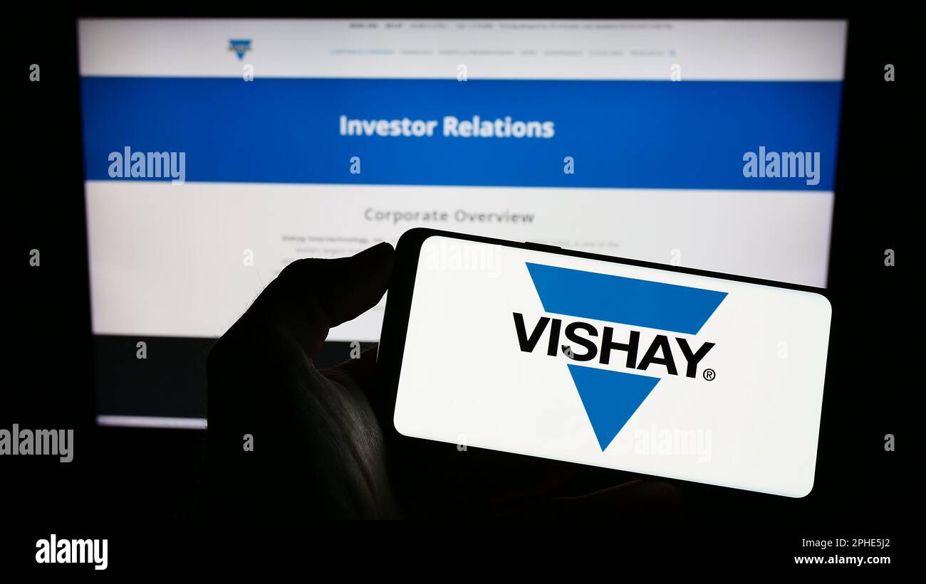 Person, die ein Mobiltelefon mit dem Logo des US-Unternehmens Vishay Intertech Inc. Auf dem Bildschirm vor der Unternehmenswebseite hält. Konzentrieren Sie sich auf das Display des Telefons. Stockfoto